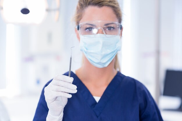 Foto dentista in maschera che tiene esploratore dentale