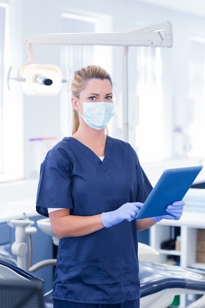 Dentist in mask using her tablet and looking at camera at the dental clinic