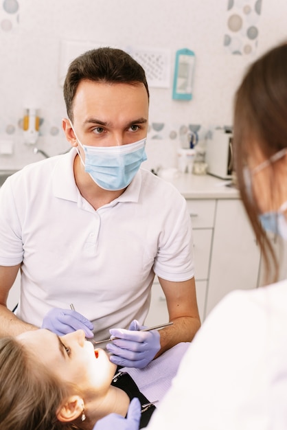 Стоматолог и медсестра, делая профессиональную чистку зубов молодой пациентки в стоматологическом кабинете.