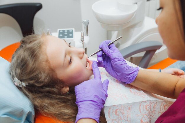 치과 의사는 귀여운 소녀에게 검사 절차를 수행합니다 치과 의사의 사무실에 앉아있는 어린 소녀