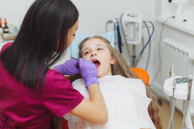 Il dentista esegue una procedura di esame su una bambina carina bambina seduta nell'ufficio del dentista