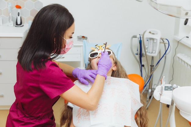 The dentist performs an examination procedure on a cute little girl Little girl sitting in the dentist's office