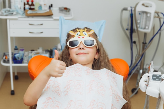 The dentist performs an examination procedure on a cute little girl Little girl sitting in the dentist's office