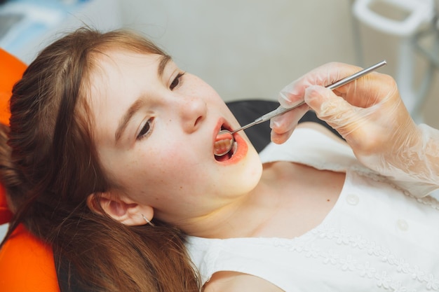 Il dentista esegue una procedura di esame su una bambina carina bambina seduta nell'ufficio del dentista