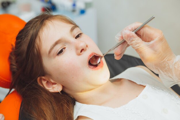 Il dentista esegue una procedura di esame su una bambina carina bambina seduta nell'ufficio del dentista