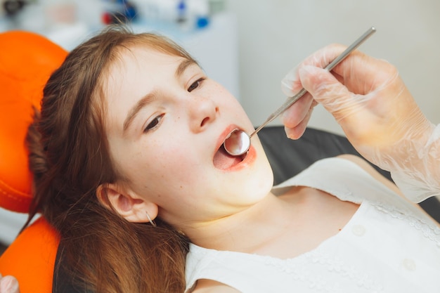 The dentist performs an examination procedure on a cute little girl Little girl sitting in the dentist's office