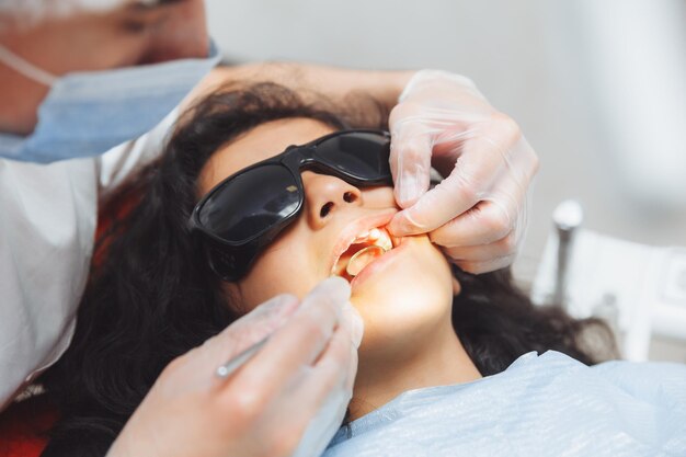 The dentist performs an examination procedure on a cute little girl Little girl sitting in the dentist's office