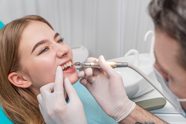 Стоматолог полирует зубы пациента с помощью дрели с щеткой