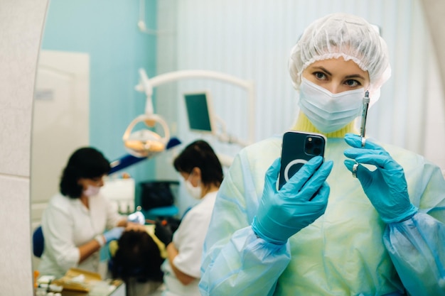 The dentist in a protective mask stands next to the patient and takes a photo after work