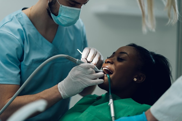 Dentist providing dental care treatment to a african american\
female patient