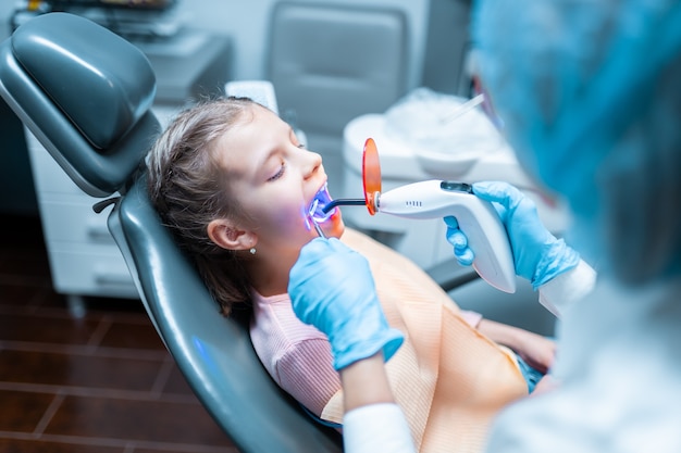 Dentista che fornisce restauro dentale e riempimento con polimerizzazione lampada uv per bambina