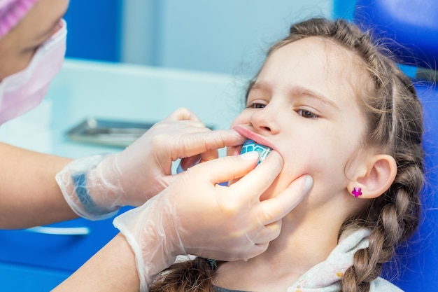 Dentist putting orthodontic trainer for little girl sitting on chair in Dentist office.