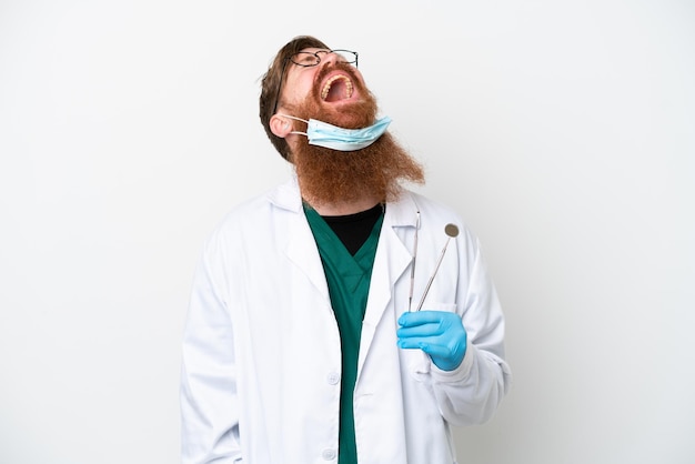 Dentist reddish man holding tools isolated on white background laughing