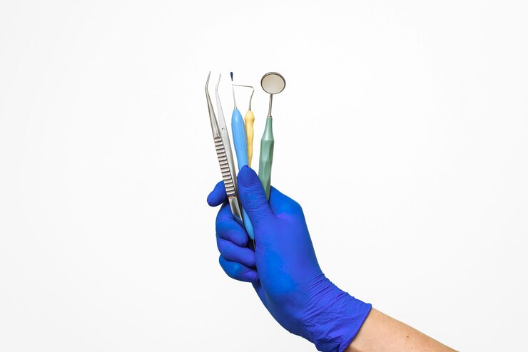 The dentist's hand in a blue glove holds dental instruments.