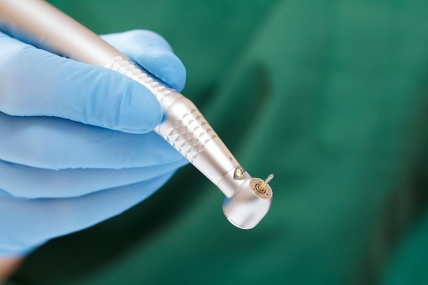 Dentist's hand in a blue latex glove with new high-speed dental handpiece on blurred background. Medical tools concept.