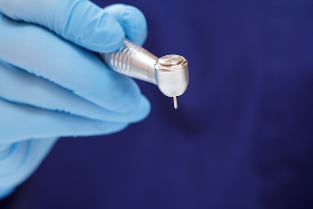 Dentist's hand in a latex glove with new high-speed dental handpiece on blurred background. Medical tools concept.