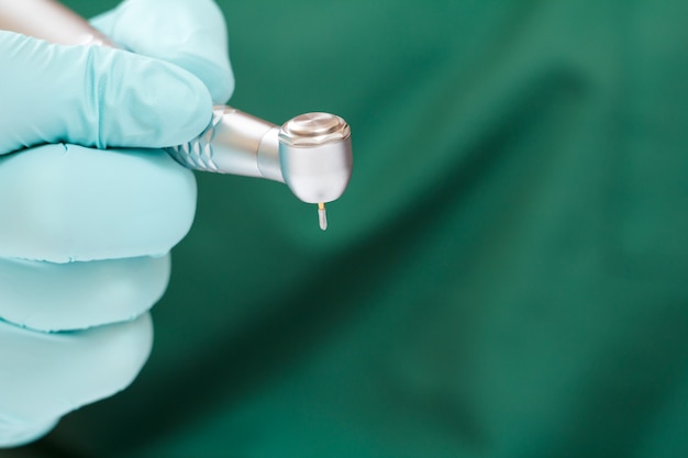 Dentist's hand in a latex glove with new high-speed dental handpiece on blurred background. Medical tools concept.