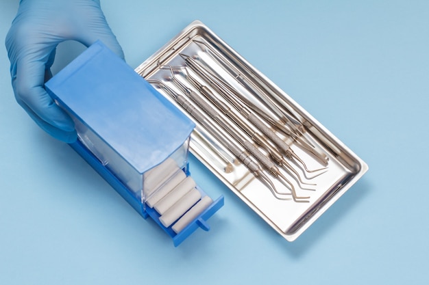 Dentist's hand in a latex glove with plastic box of cotton tampons, set of composite filling instruments for dental treatment in steel tray. Medical tools concept. Top view.