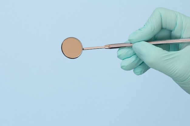 Dentist's hand in a rubber glove with mouth mirror on blue background. Medical tools concept.