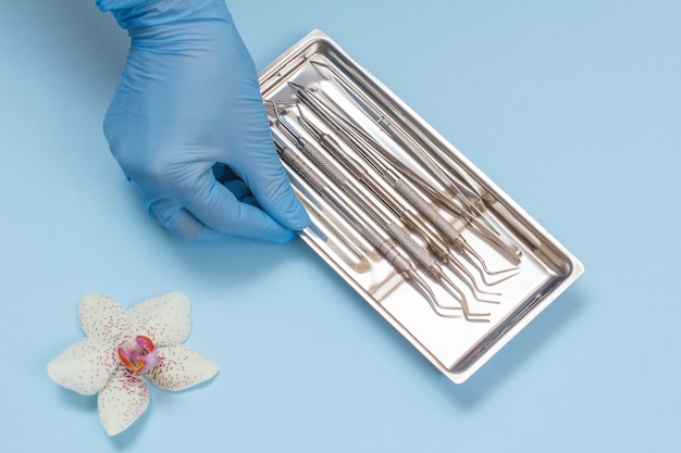 Dentist's hand in a rubber glove with set of composite filling instruments for dental treatment in steel tray. Medical tools concept. Top view.