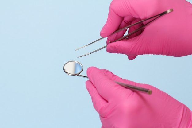 Dentist's hands in pink latex gloves with tweezers and mouth mirror on blue background. Medical tools concept.