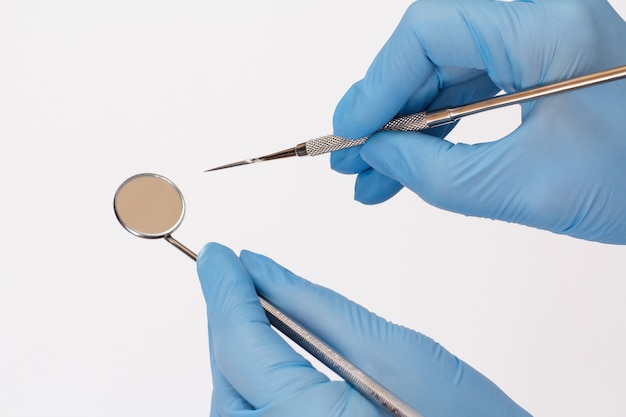 Dentist's hands in rubber gloves with probe and mouth mirror on white background. Medical tools concept. Top view.