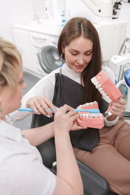 Dentist showing how to brush teeth on dental model to her female patient