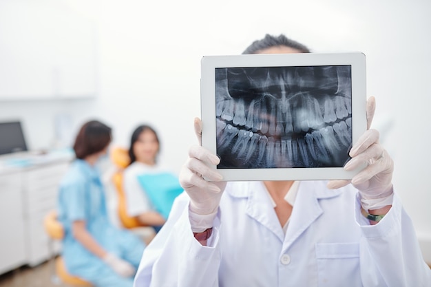 Dentist showing tablet computer with jaw x-ray of female patient on screen