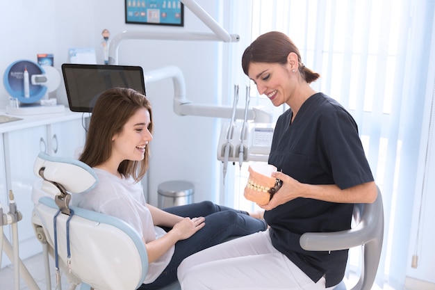 Photo dentist showing teeth model to smiling patient in clinic