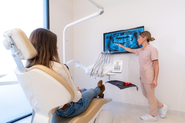 Photo dentist showing xray on monitor to young client in modern dental clinic