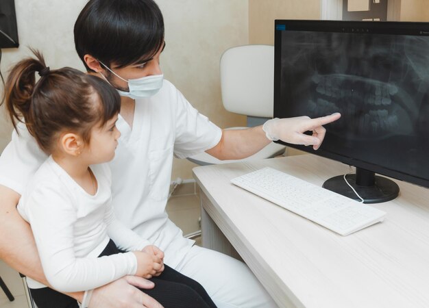 치과 의사는 환자에게 컴퓨터에서 치아의 어린 소녀 엑스레이를 보여줍니다