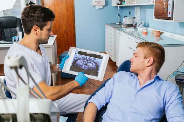 A dentist shows the patient an X-ray image of his teeth on the screen.