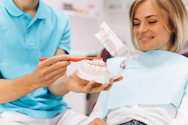 Foto il dentista mostra alla donna sul modello come lavarsi i denti correttamente