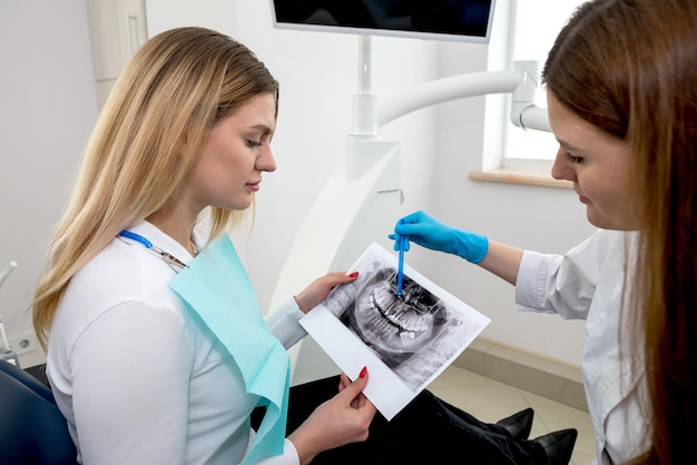 The dentist shows the xray image to the patient People medicine dentistry technology and healthcare concept Woman dentist with xray image of teeth and female patient in dental clinic office