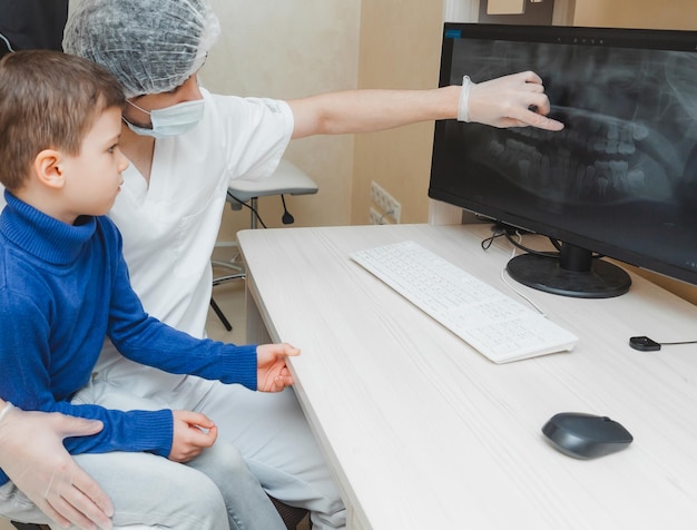 The dentist shows the xray of the teeth on the computer to the patient boy