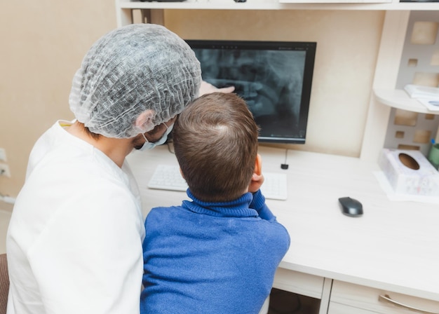 The dentist shows the xray of the teeth on the computer to the patient boy