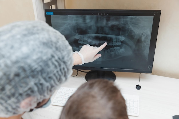 歯科医は患者の男の子にコンピューターの歯のレントゲン写真を見せます