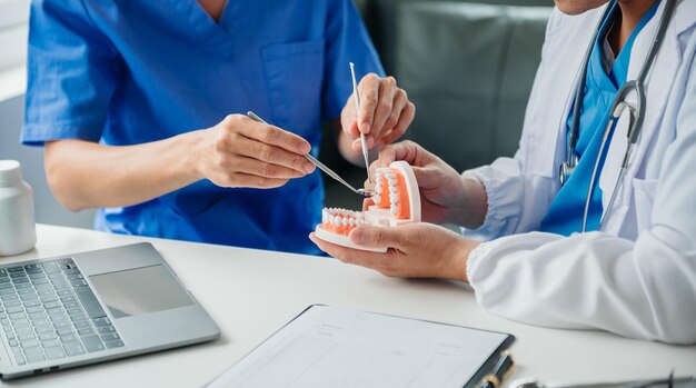 Photo dentist sitting at table with jaw samples tooth model and working with tablet and laptop in dental office professional dental clinic medical doctor workingxa