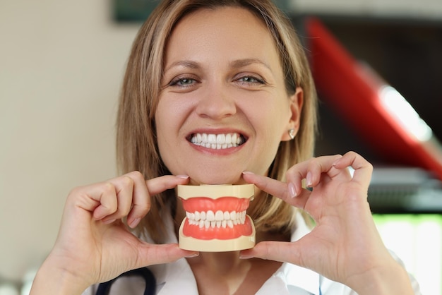 Dentist smiles and shows plastic jaws in her hands woman stomatologist holding artificial teeth