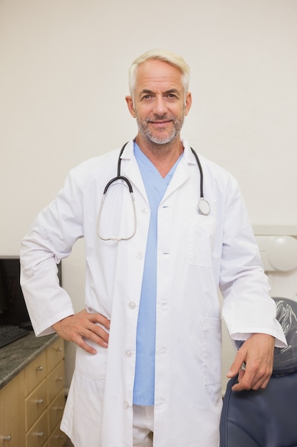 Photo dentist smiling at camera beside chair