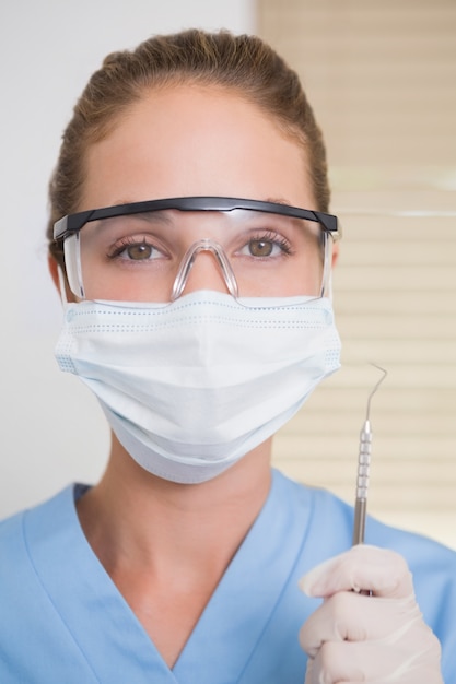 Dentista in maschera chirurgica tenendo esploratore dentale