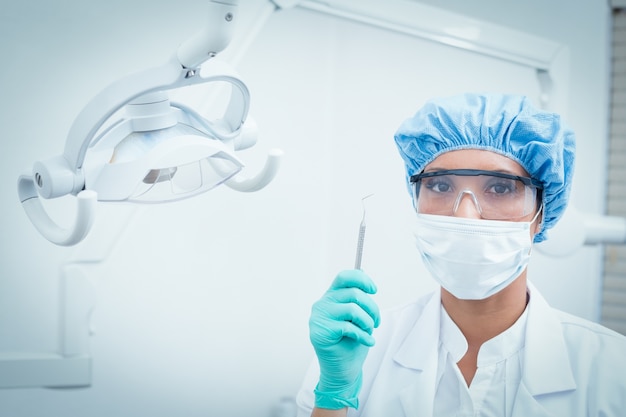 Dentista in maschera chirurgica e occhiali di sicurezza in possesso di gancio