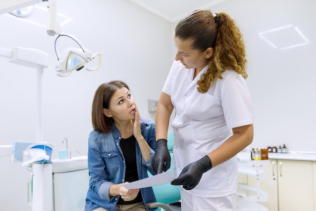 Стоматолог, говорить с женщиной пациента в стоматологическом кресле.