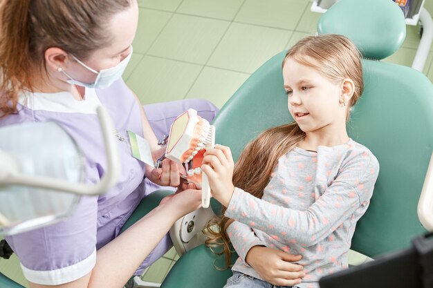 Foto dentista che insegna alla ragazza come lavarsi i denti. dentista pediatrico che istruisce un bambino sullo spazzolamento dei denti su un modello.