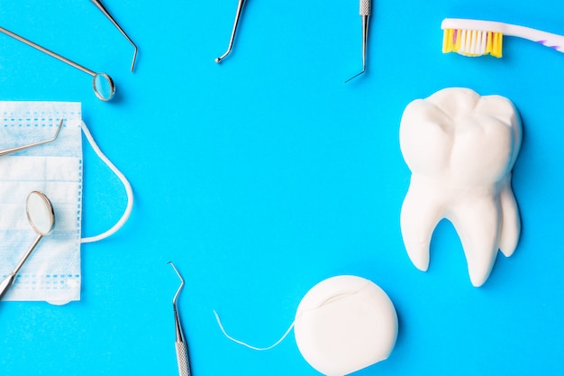 Dentist tools or instruments dental explorers, dental mirrors, toothbrush, dental floss and procedure face mask on light blue background.