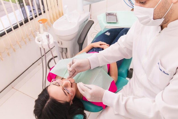 사진 치과 의사는 치과 사무실에서 젊은 여성 환자를 치료하고 있습니다.