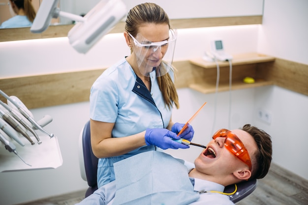Dentist treating a patient with dental ultraviolet curing light\
tool.
