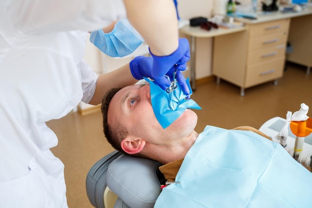 Dentist during the treatment of a male patient. Female dentist in face mask with male patient sitting in dentist chair sitting in dental clinic. Selective focus