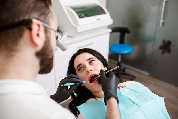 Стоматолог лечит зубы с помощью стоматологического микроскопа и инструментов. Испуганный пациент у стоматолога.