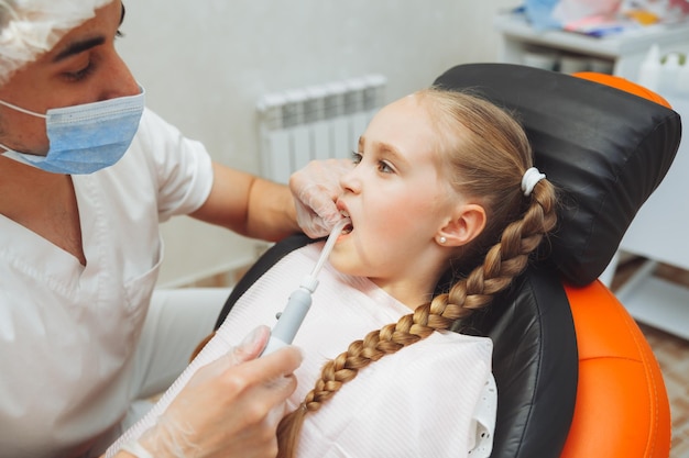 A dentist treats a little girl's teeth with dental equipment Dental treatment in children Dentistry and Orthodontics